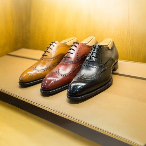 Trois paires de souliers habillés en cuir, en beige, brun et noir, exposés sur une étagère en bois