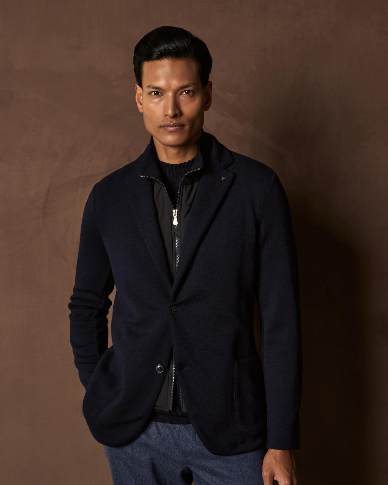 Man wearing a navy blazer with a black zip-up vest underneath