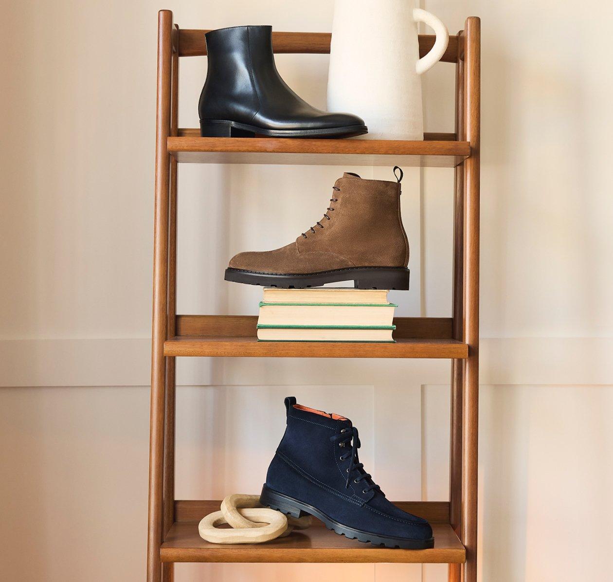 Trois modèles de bottines sur une étagère : une bottine en cuir noir, une bottine en suède brun à semelle crantée, et une bottine en suède noir à lacets