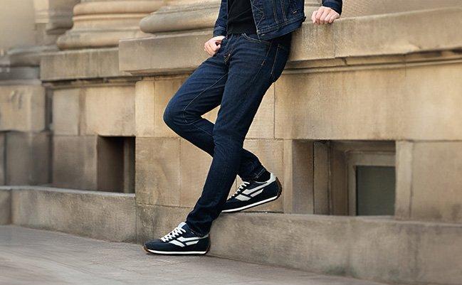 A man wearing a dark blue jeans with black sneakers