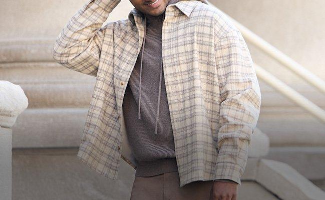 Man wearing a beige plaid overshirt layered over a dark hoodie