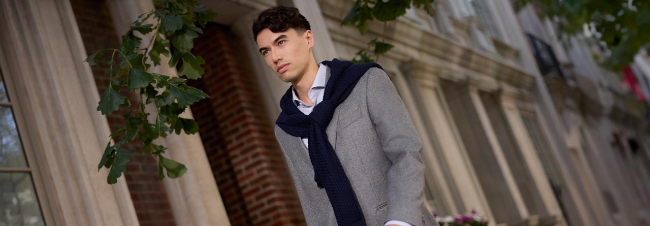 A man wearing a grey sport jacket with grey shirt and black scarf