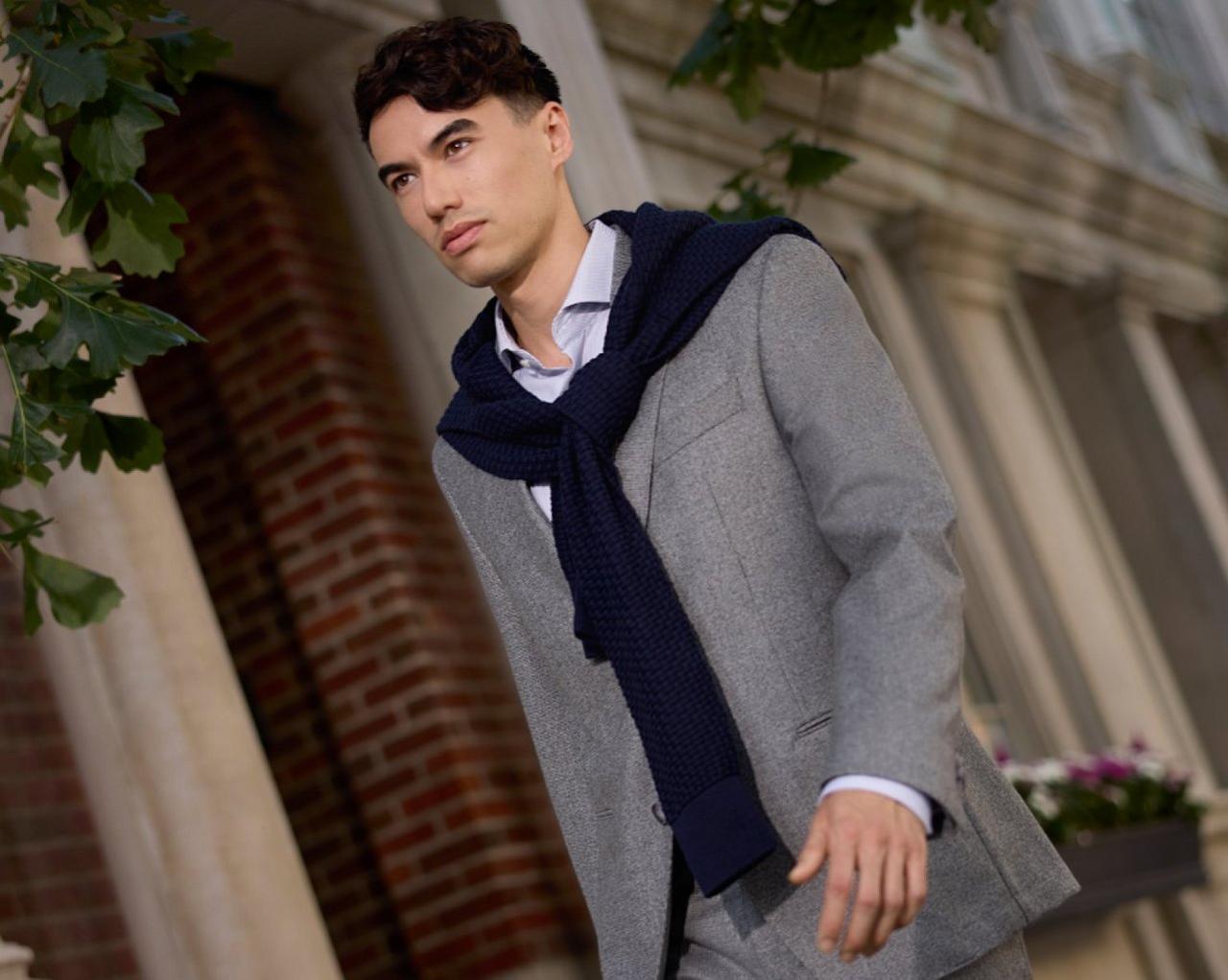 A man wearing a grey sport jacket with grey shirt and black scarf