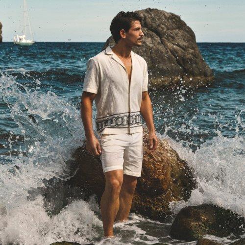 Man by the sea wearing a lightweight outfit, representing tropical travel essentials