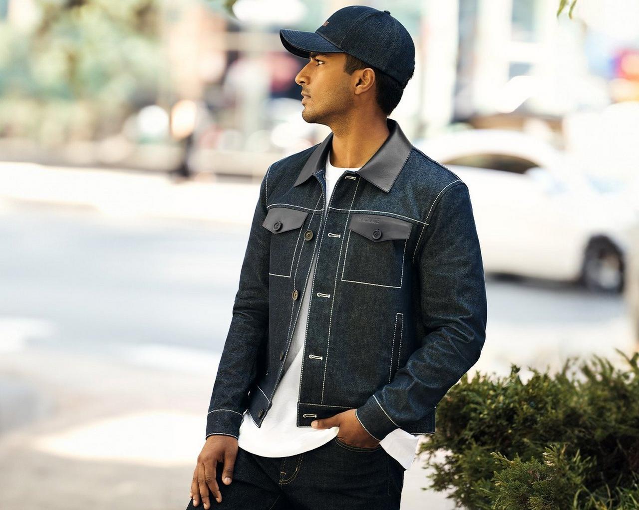 Homme portant une veste en denim foncé avec une casquette assortie, superposée sur un t-shirt blanc et un jean foncé, debout à l’extérieur
