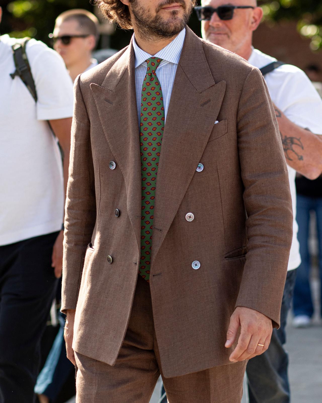 Homme portant un complet croisé brun avec une cravate verte à motifs