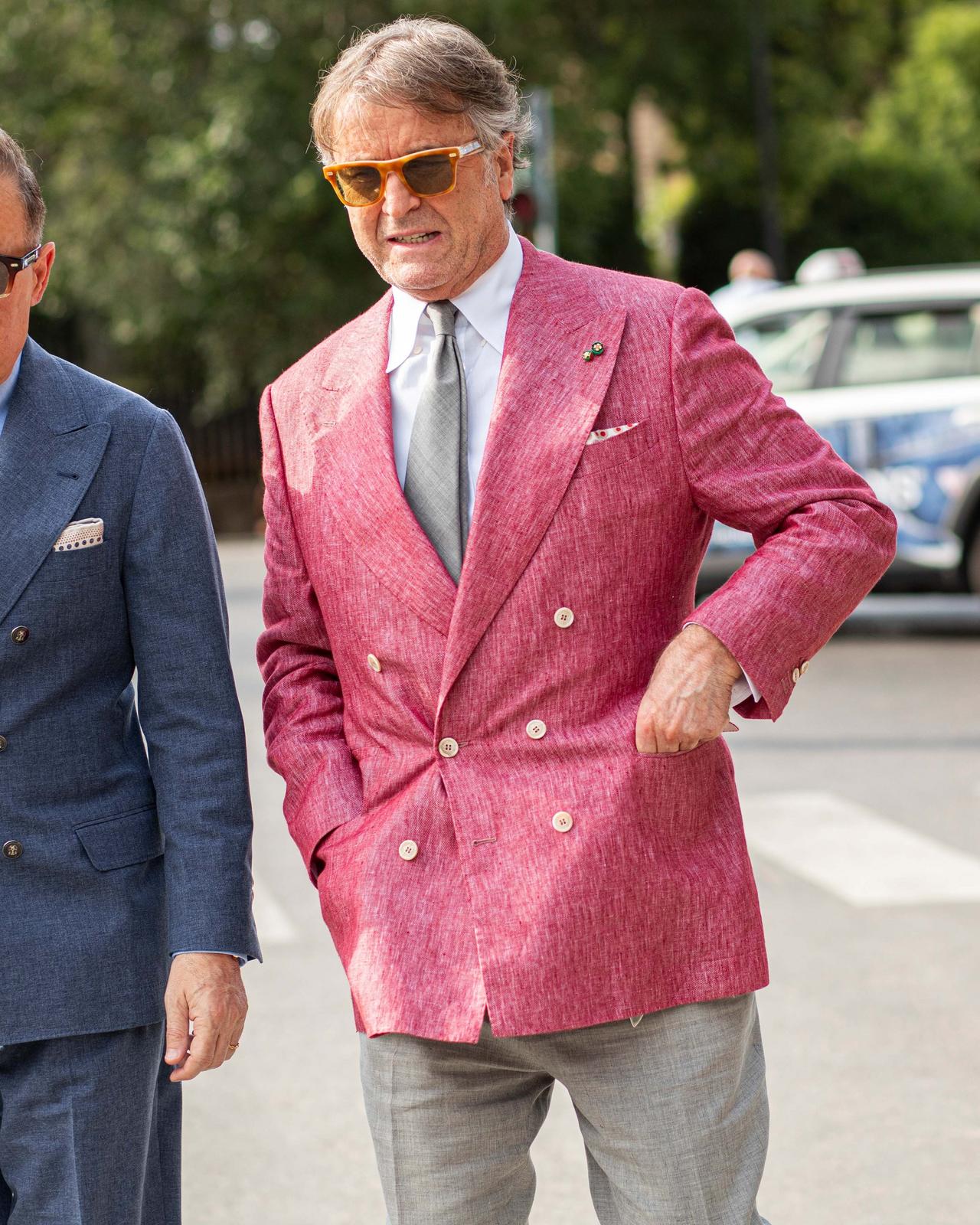 Man wearing a bright pink double-breasted blazer with a grey tie and light trousers, walking outdoors