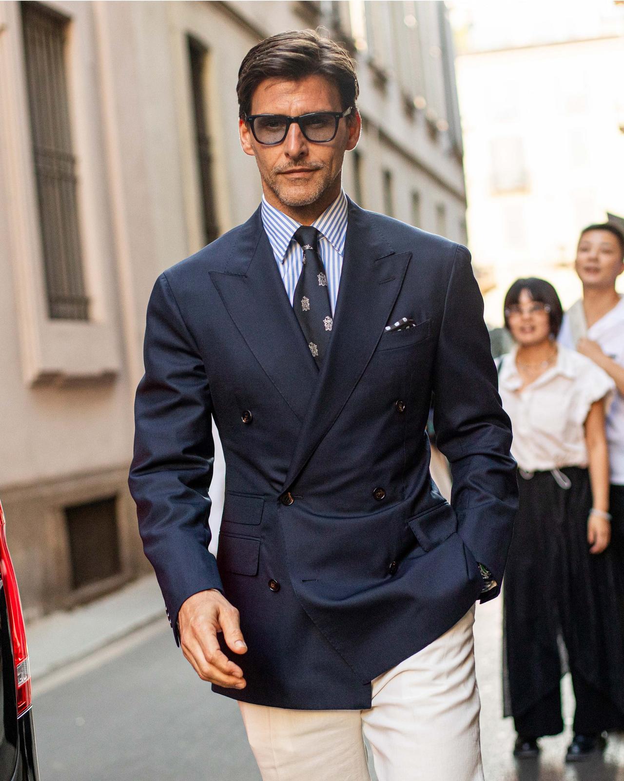 Homme portant un veston croisé bleu marine avec une chemise à rayures, une cravate à motifs et un pantalon blanc