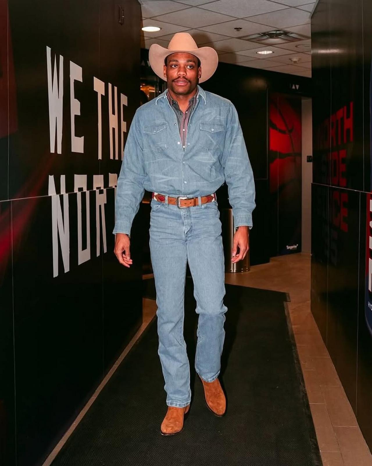 Un homme déguisé en cowboy portant un chapeau beige, une chemise en denim, un jean et des bottes brunes