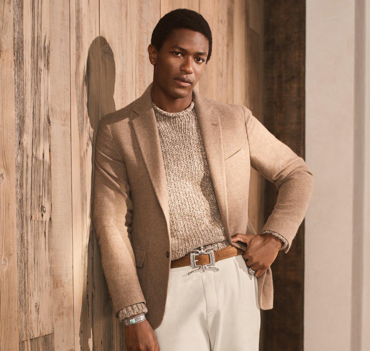 Un mannequin portant une veste sport Ralph Lauren Purple Label brun pâle, un tricot, une ceinture en cuir fauve et un pantalon blanc