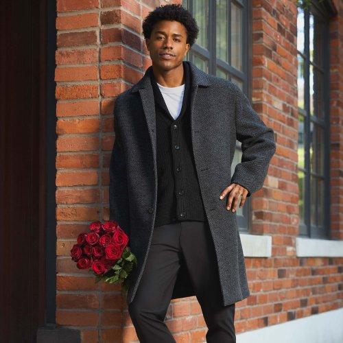 Un mannequin masculin porte un manteau gris, un cardigan noir et un t-shirt blanc, assortis d’un pantalon noir