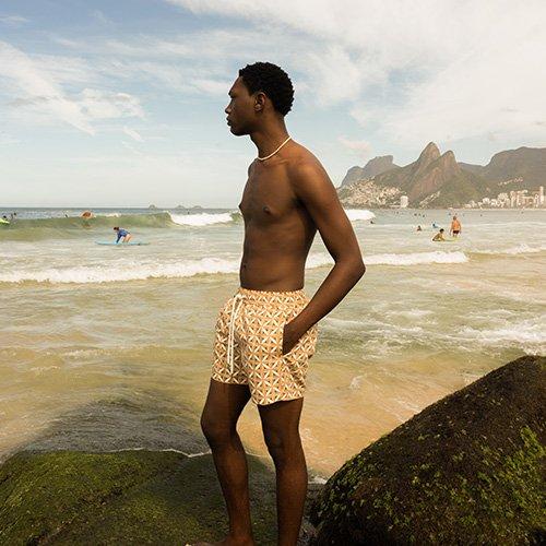 Male wearing swim trunks on the beach signifying swimwear labels to know
