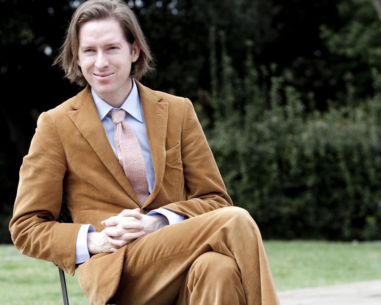 Wes Anderson en complet brun avec une chemise bleu pâle et une cravate rose pâle