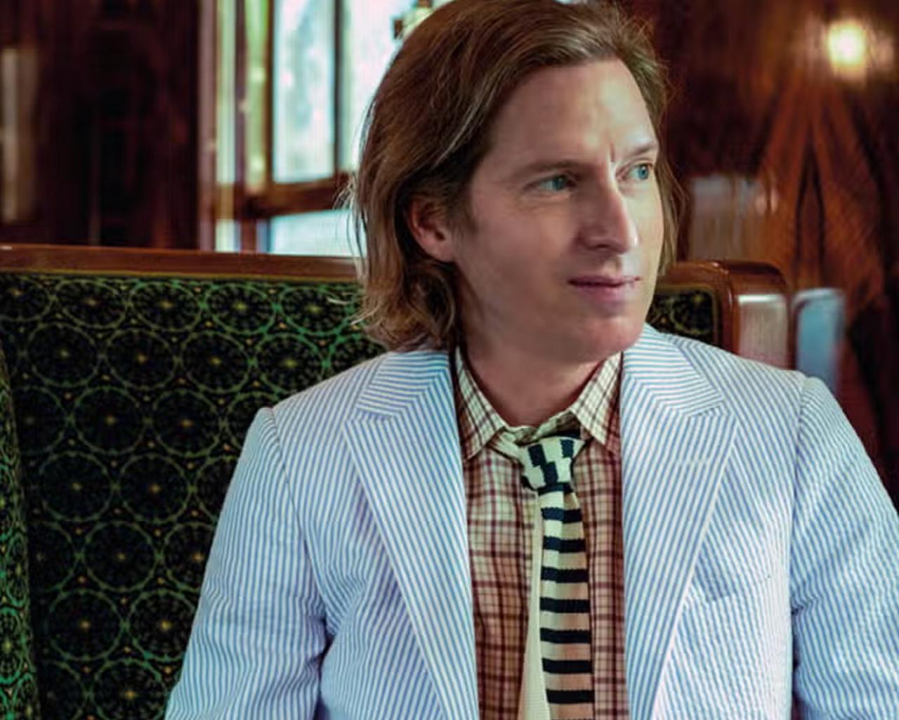 Wes Anderson wearing a light blue pinstripe blazer over a checked shirt with a striped tie