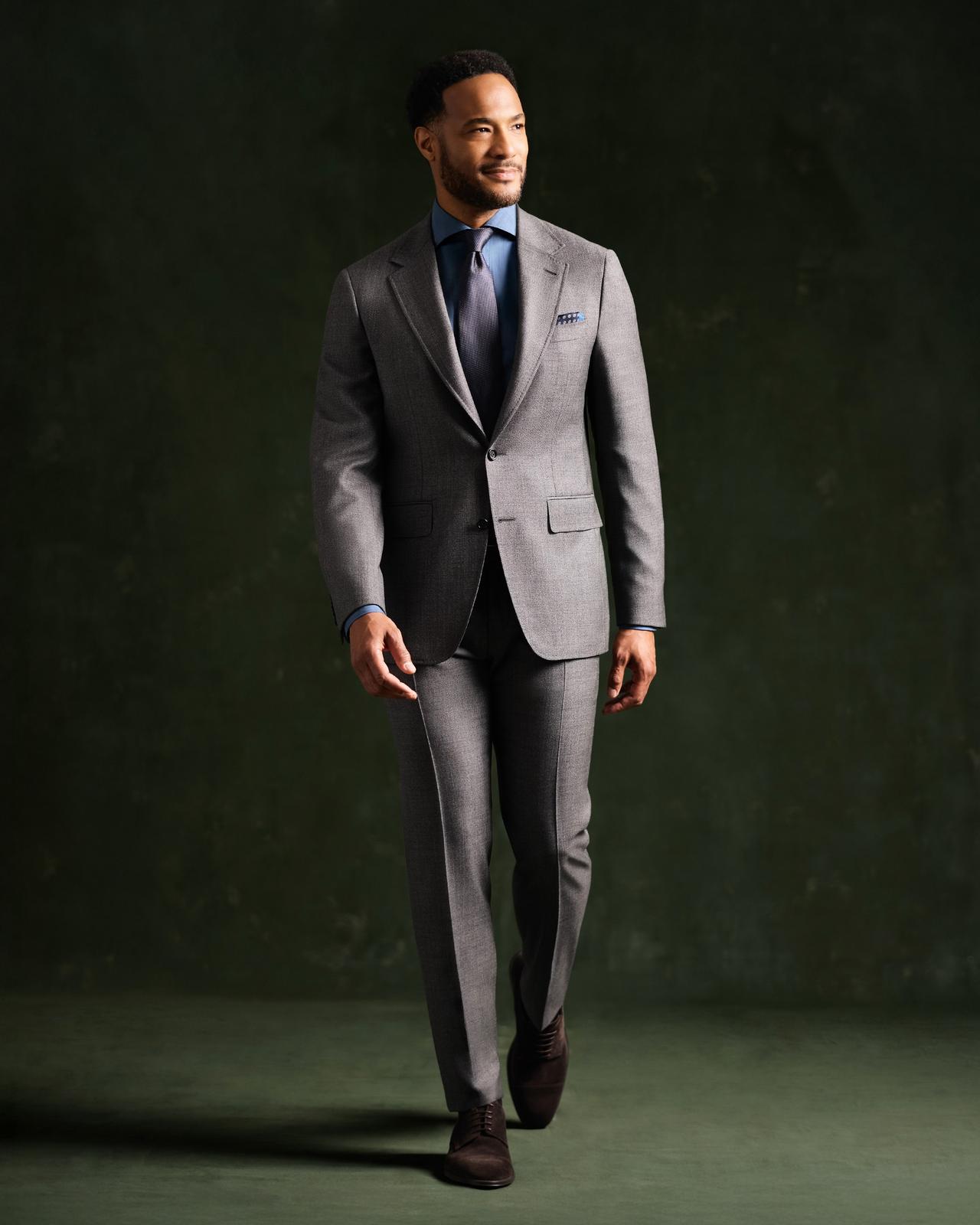 Un mannequin masculin portant un complet gris Canali et une cravate bleue, en train de marcher