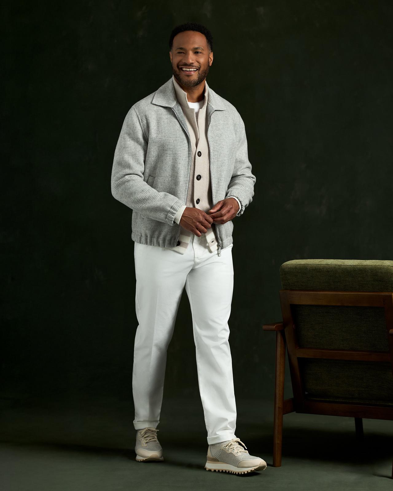 Modèle masculin portant une veste Eleventy et un pantalon blanc, debout à côté d’une chaise