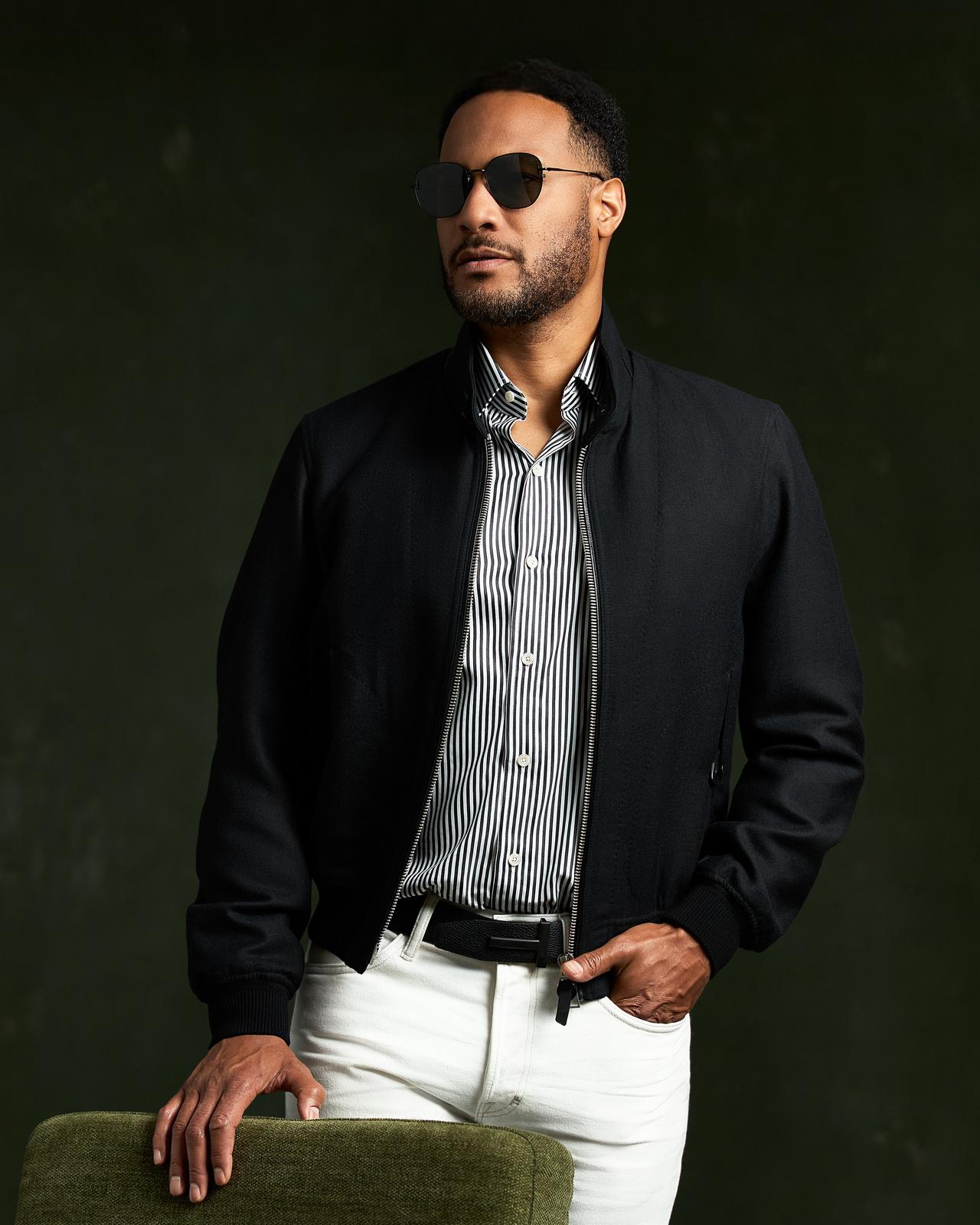 Modèle masculin portant une veste TOM FORD et un pantalon blanc, debout à côté d’une chaise