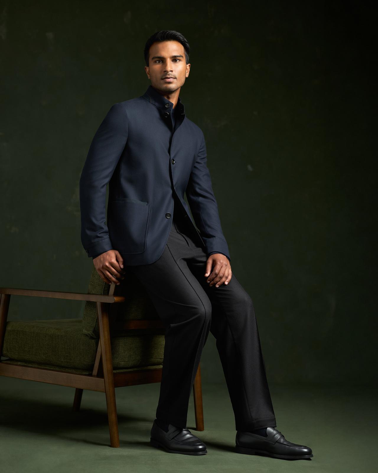 Modèle masculin portant un costume bleu marine ZEGNA, assis sur une chaise