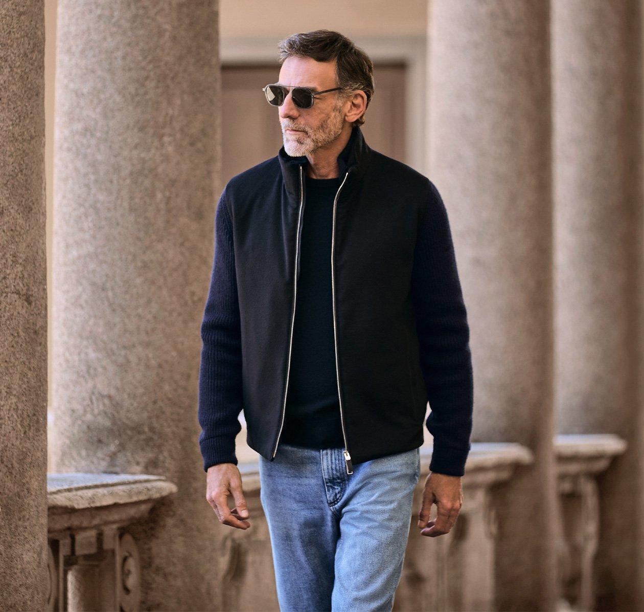 A man wearing a Zegna jacket layered over a black sweatshirt and paired with blue jeans