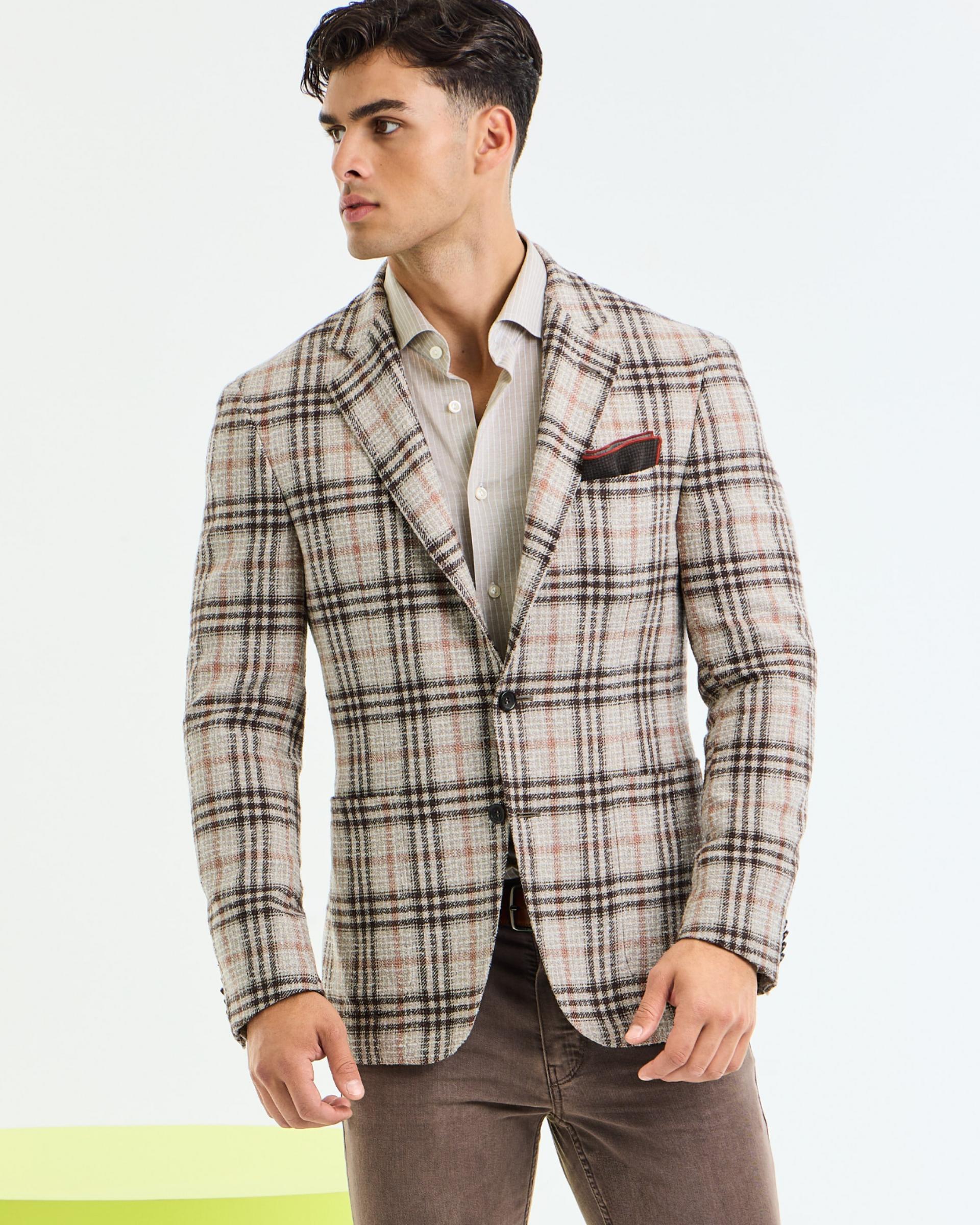 A man wearing a beige plaid sports jacket layered over a light dress shirt