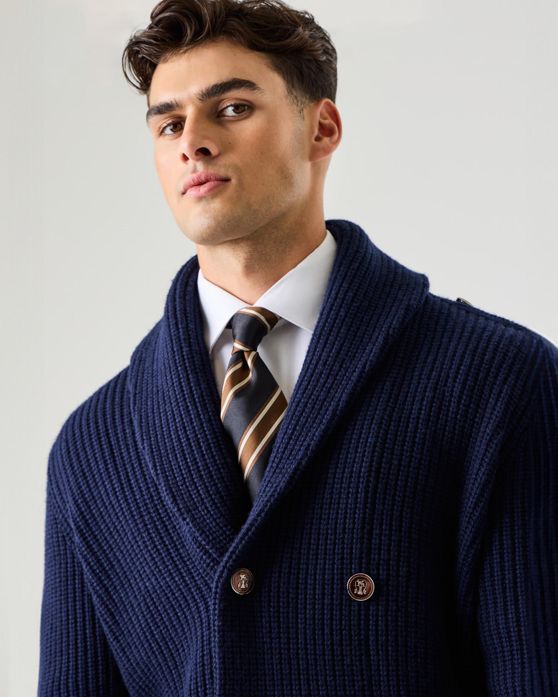 A man wearing a navy sweater layered over a dress shirt and striped tie