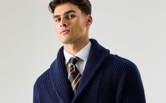 Un homme portant un chandail bleu marine superposé à une chemise et une cravate à rayures
