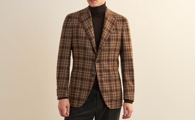 A man wearing a brown plaid sports jacket layered over a black turtleneck