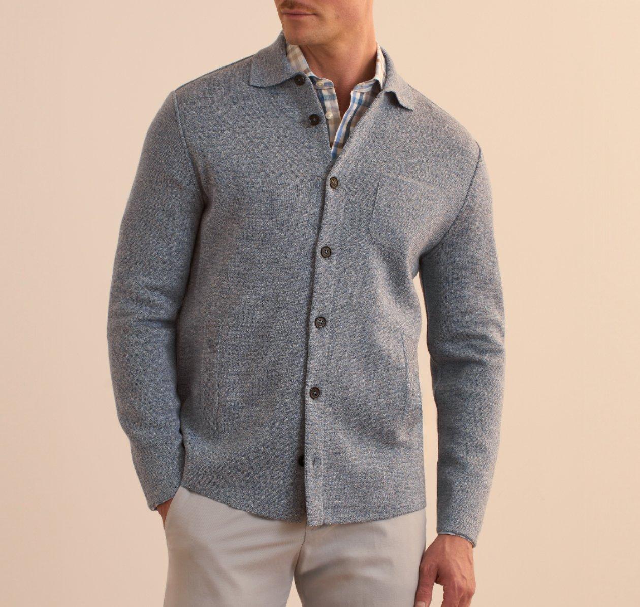 Un homme portant un cardigan gris pâle à boutons superposé à une chemise à carreaux