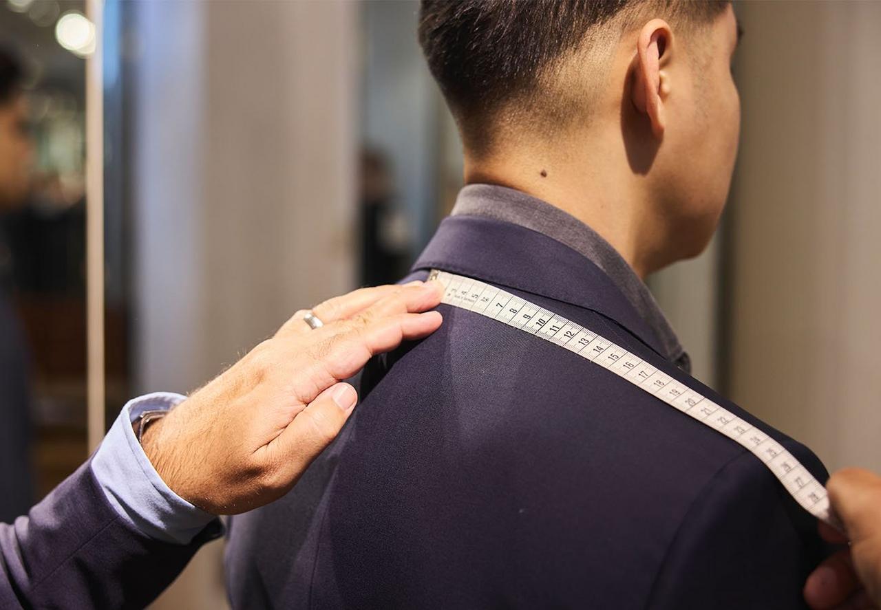 Homme essayant une veste sport pendant qu’un conseiller de style prend ses mesures