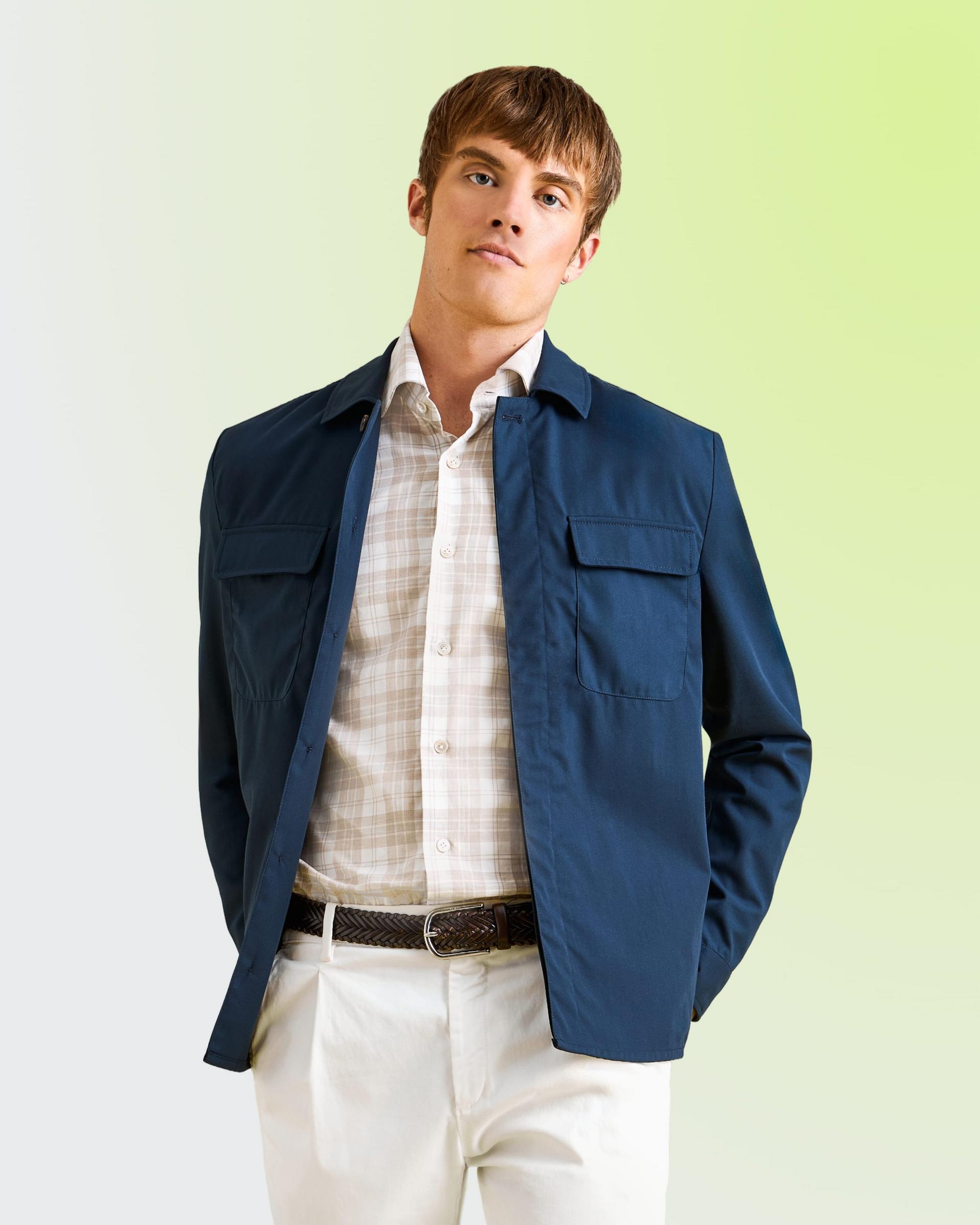 Un homme portant une veste bleu marine, une chemise à carreaux et un pantalon blanc