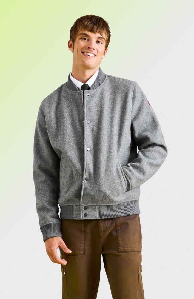 a man wearing a grey button-up bomber jacket paired with brown pants and a collared shirt 