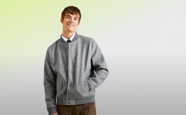 a man wearing a grey button-up bomber jacket paired with brown pants and a collared shirt 