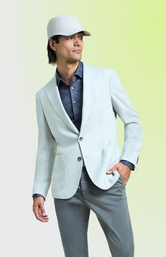 Man wearing a light blue blazer, blue button-up shirt, grey trousers, and a white baseball cap.