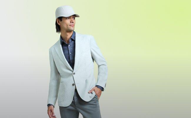 Homme portant un veston bleu pâle, une chemise boutonnée bleue, un pantalon gris et une casquette de baseball blanche.