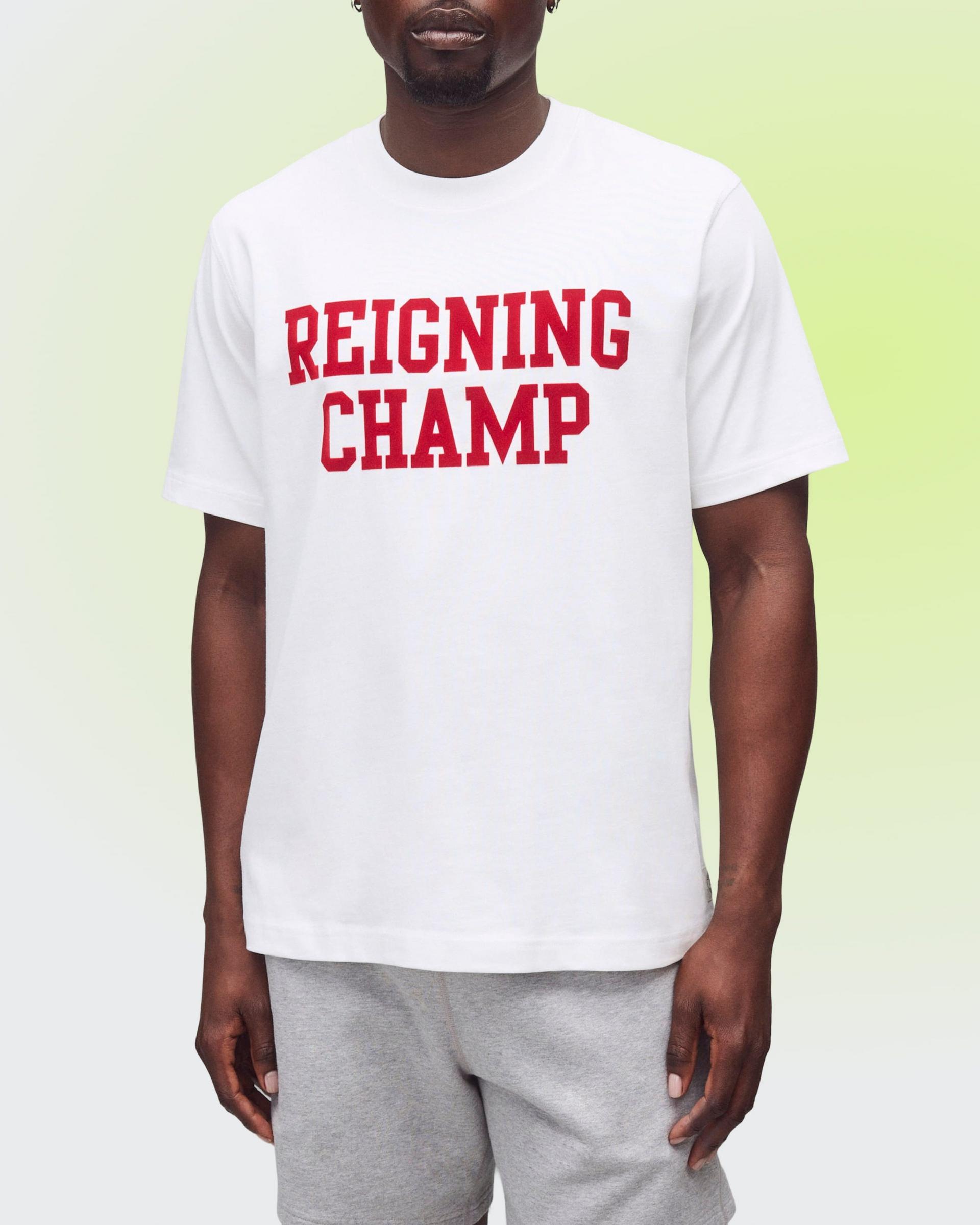 Man wearing a white T-shirt with red “REIGNING CHAMP” lettering and grey sweatpants