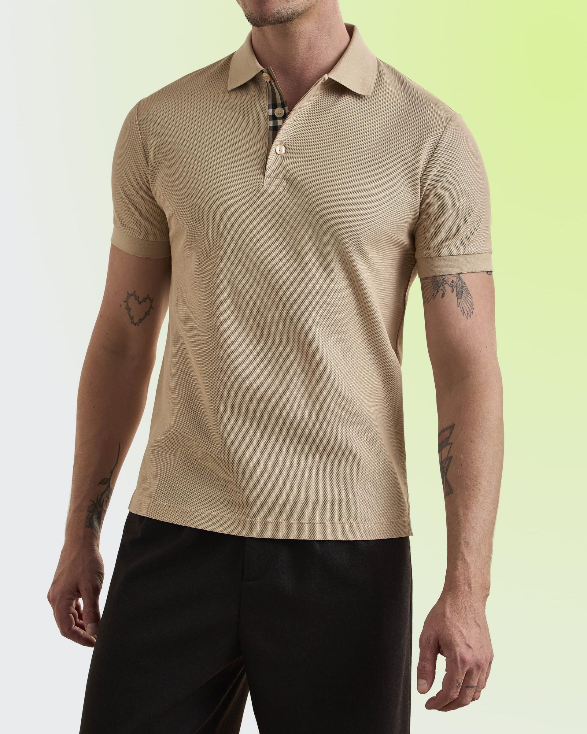 A man wearing a beige short-sleeve polo shirt with a ribbed texture and a partially unbuttoned collar revealing a checkered inner lining