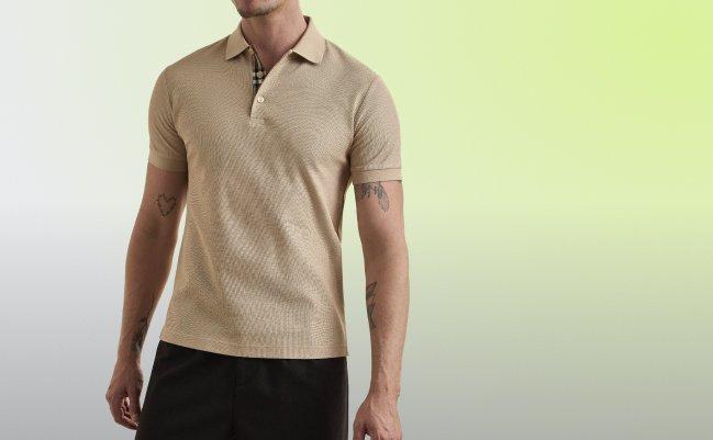 Un homme portant un polo beige à manches courtes, à la texture côtelée, avec le col partiellement déboutonné laissant voir une doublure intérieure à carreaux