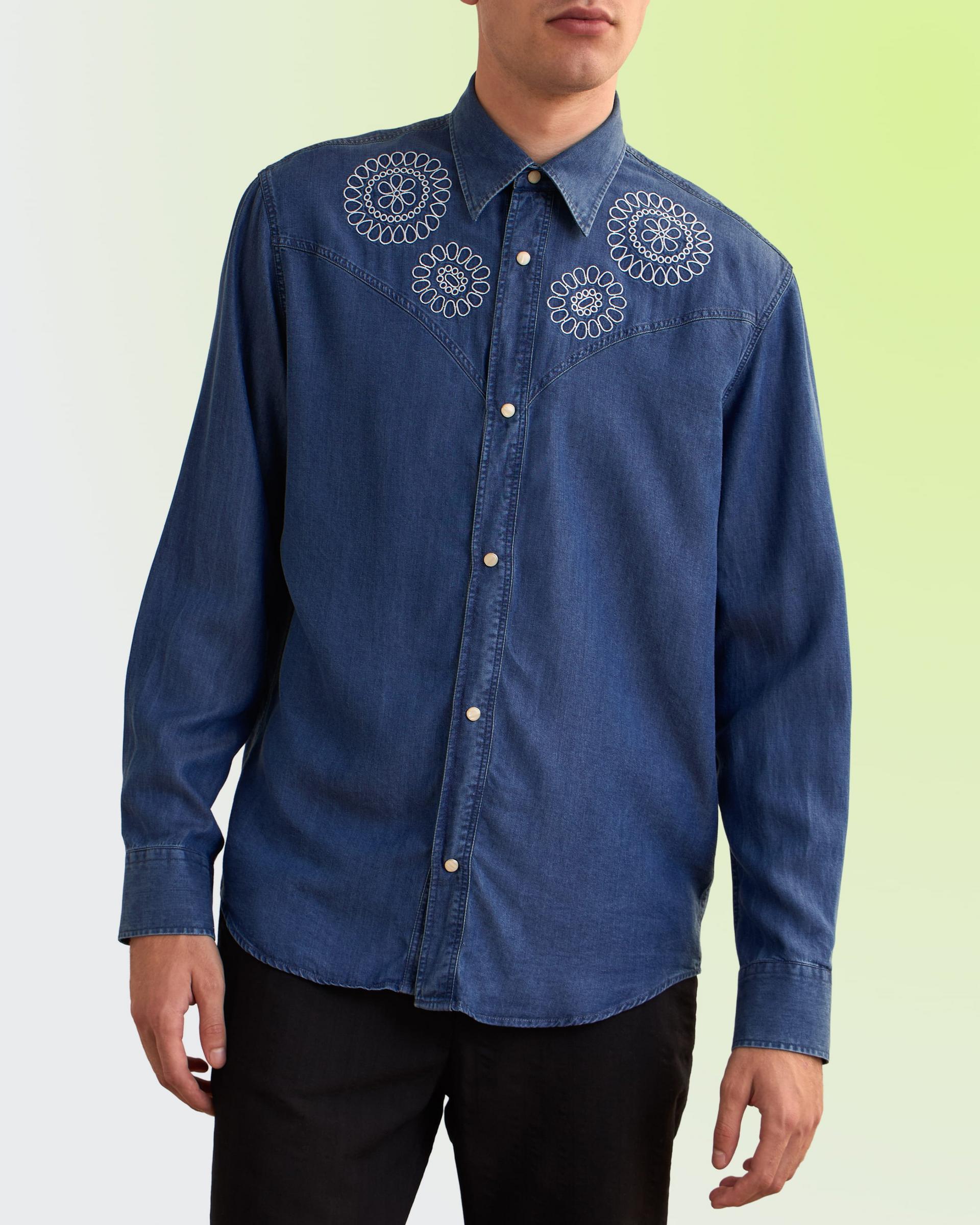  A man wearing a blue denim button-up shirt with intricate white circular embroidery on the chest