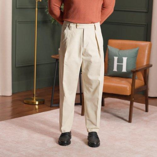A man wearing an off-white dress pants with black shoes and light brown sweater 