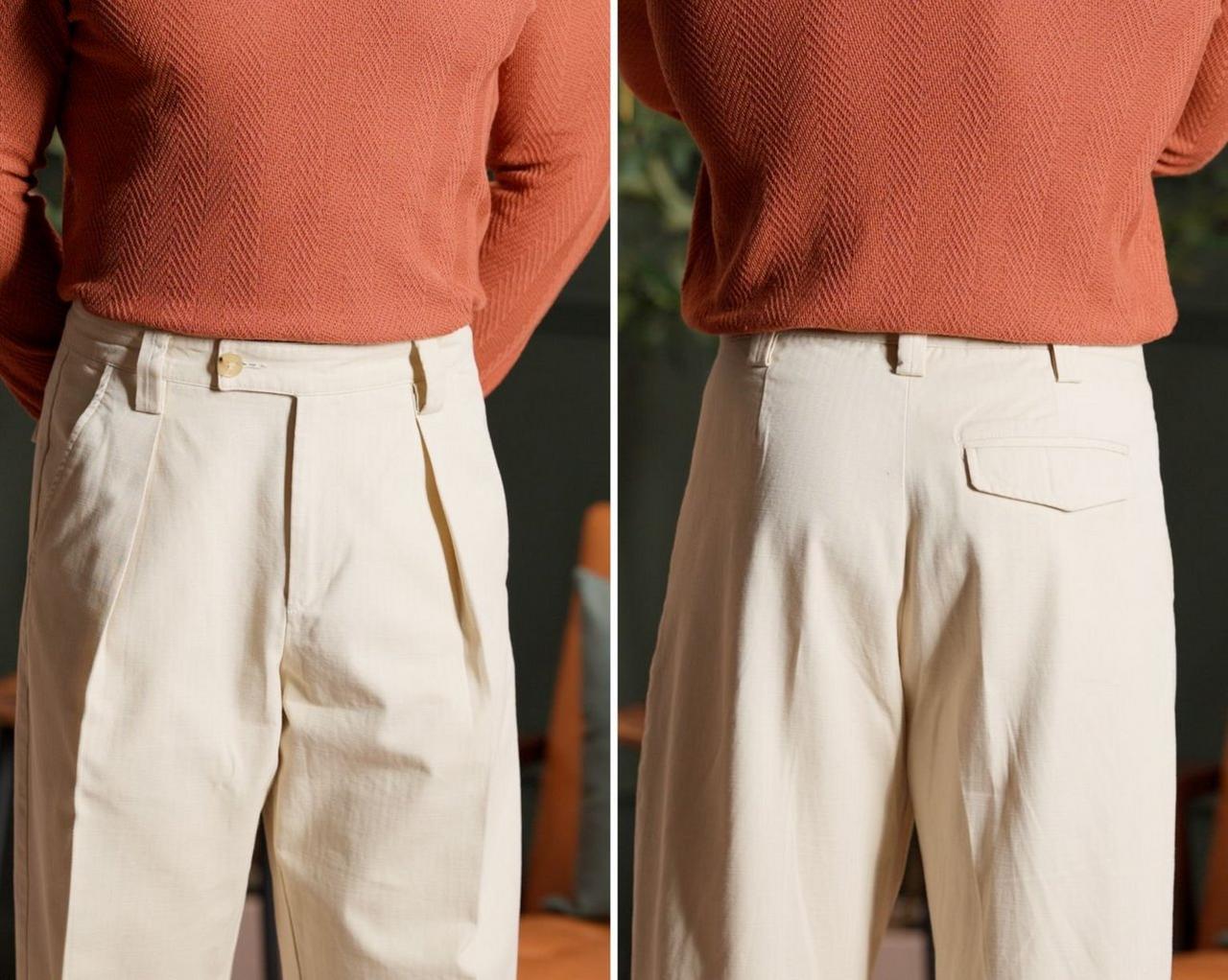 a person wearing a rust-colored sweater paired with cream pleated trousers, viewed from the front and back 