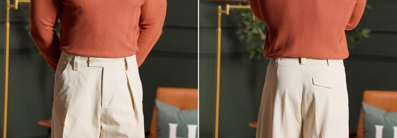 a person wearing a rust-colored sweater paired with cream pleated trousers, viewed from the front and back 