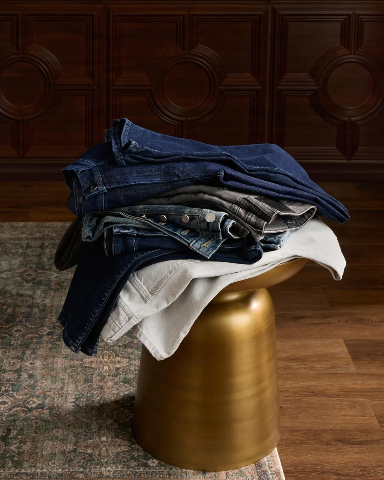 Piles de jeans en denim et de pantalons crème pliés sur un tabouret doré