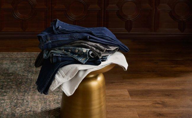 Piles de jeans en denim et de pantalons crème pliés sur un tabouret doré