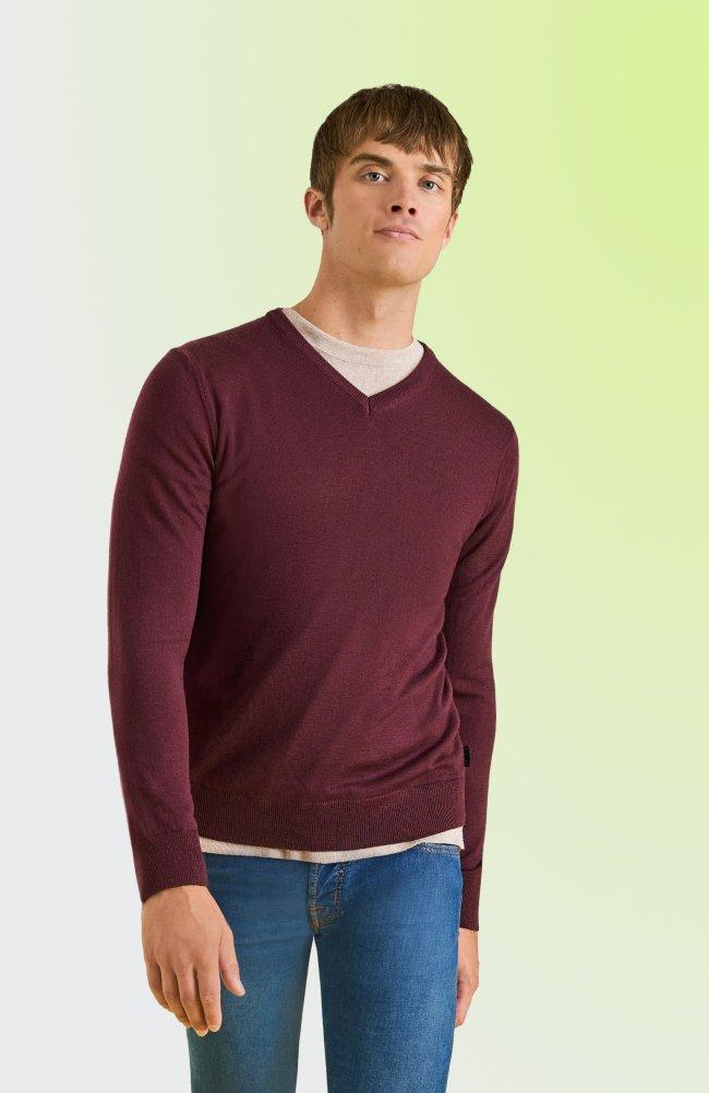 Homme portant un chandail bordeaux à col en V par-dessus un T-shirt beige et un jean bleu