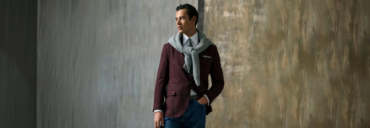 model dressed in a burgundy checkered blazer, white dress shirt, and a light gray scarf, paired with blue jeans