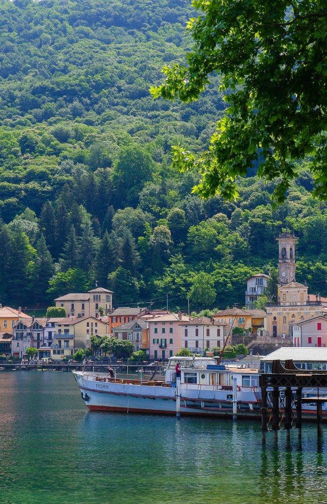 Lakeside Italian village with colourful buildings and a bell tower, boats docked at a pier, Made in Italy, FW26