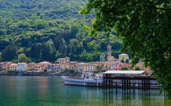 Lakeside Italian village with colourful buildings and a bell tower, boats docked at a pier, Made in Italy, FW26