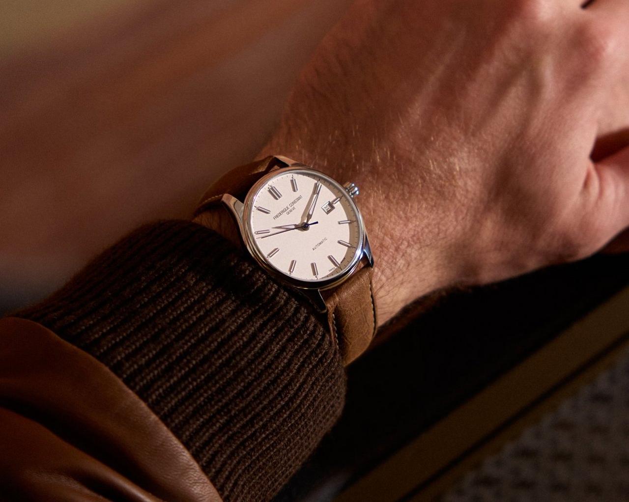 Un poignet orné d’une montre-bracelet analogique dotée d’un cadran blanc, d’index horaires en chiffres romains et d’un bracelet en cuir brun