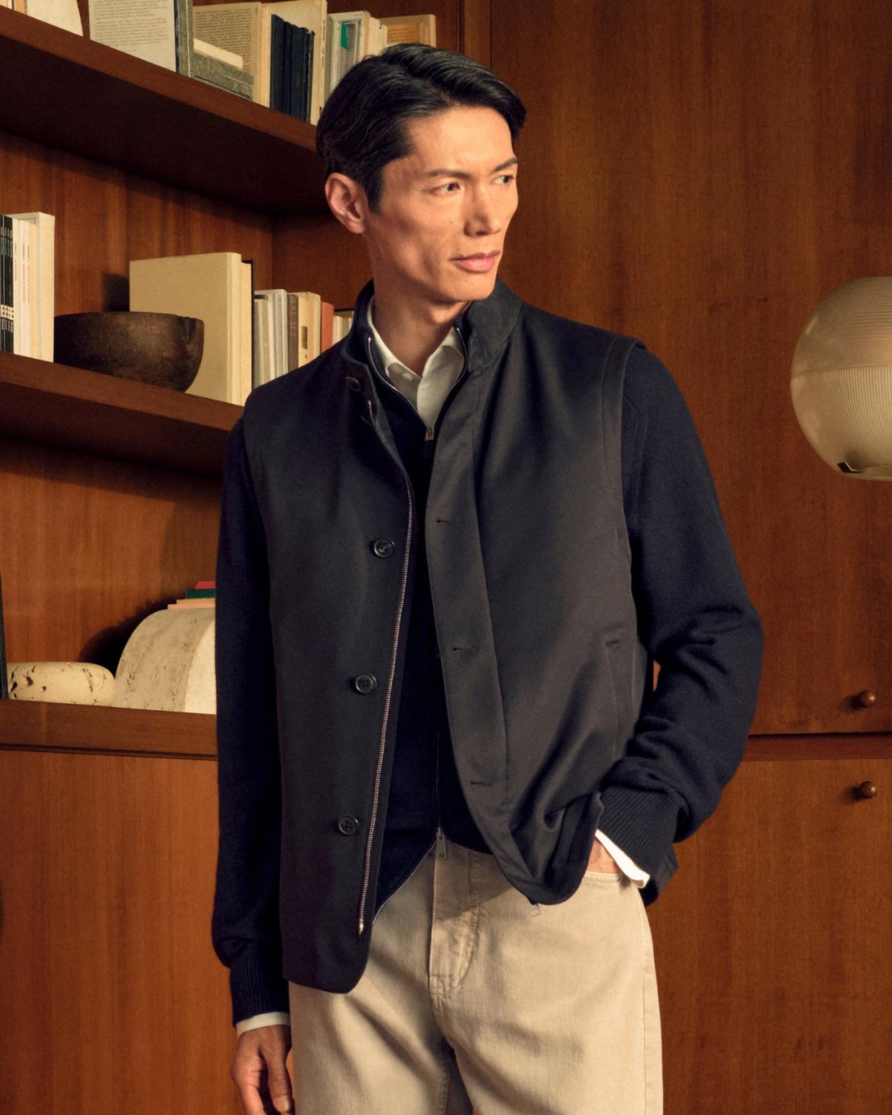 A man wearing a Gabardine Jacket in a dark navy color, paired with a white collared shirt and light-colored trousers