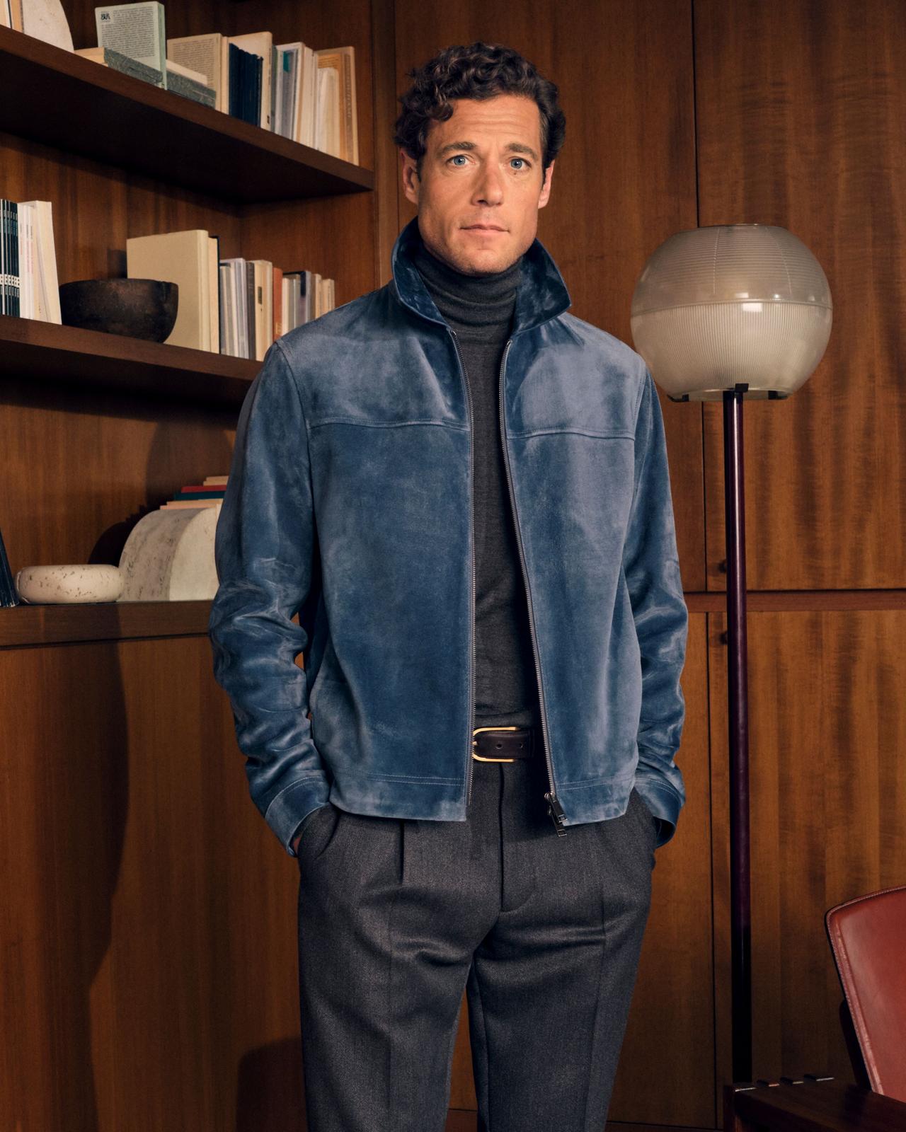 A man wearing a Gabardine Jacket in a dark navy color, paired with a white collared shirt and light-colored trousers
